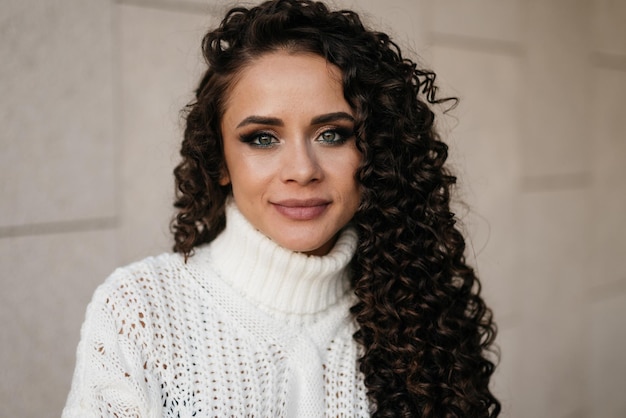 Closeup Girl en un suéter blanco con lujosos ojos verdes y cabello oscuro y rizado lindas sonrisas