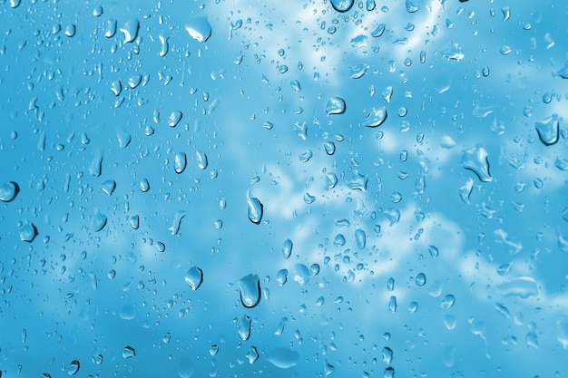 Closeup gotas de lluvia en el cristal de la ventana. Cielo azul nublado en el fondo.