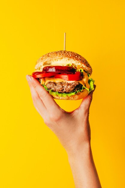 closeup de una hamburguesa en la mano de una mujer en un fondo amarillo