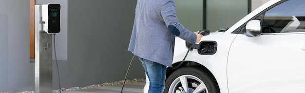 Foto closeup homem asiático progressivo recarrega seu carro ev na estação de carregamento em casa