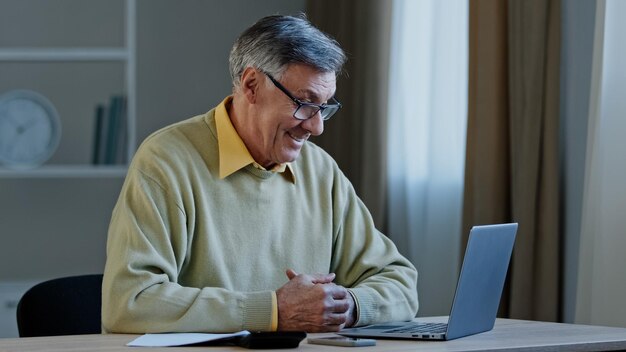 Closeup homem idoso negociando uso on-line professor de laptop ensinando palestra na internet sentado em casa mostrando o polegar para cima satisfaz o trabalho escritor maduro aposentado discute artigo sobre consulta na web do dispositivo