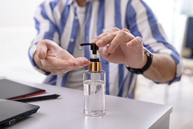 Closeup homem limpando as mãos com desinfetante, gel antibacteriano de limpeza para as mãos, trabalho remoto no laptop em casa conceito