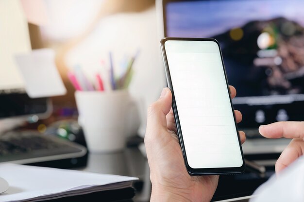 Closeup homem usando smartphone com tela em branco enquanto está sentado na mesa do escritório