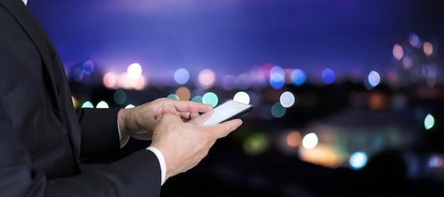 Closeup imagem de mãos masculinas usando smartphone à noite na rua comercial da cidade