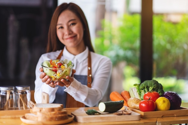 Closeup imagem de um chef feminino cozinhando e segurando uma salada de legumes frescos na cozinha