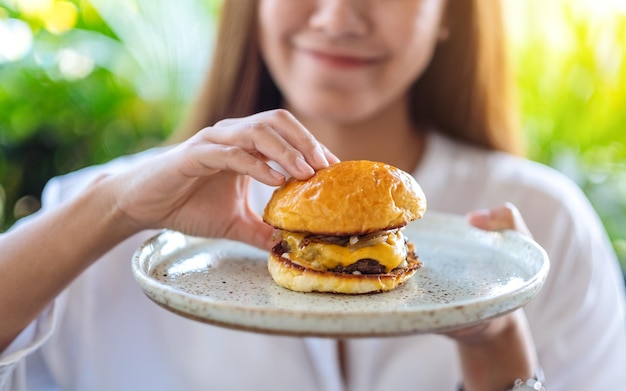 Closeup imagem de uma linda mulher agarrando e comendo hambúrguer de carne em um prato