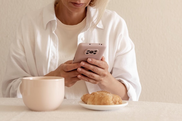 Closeup imagem de uma linda mulher sentada no interior de casa aconchegante e usando as mãos femininas do dispositivo smartphone moderno digitando mensagem de texto via conceito de rede social de celular