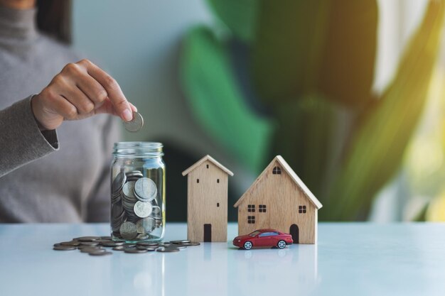 Closeup imagem de uma mulher coletando e colocando moedas em uma jarra de vidro com modelos de casas de madeira e modelo de figura de carro para economizar dinheiro conceito