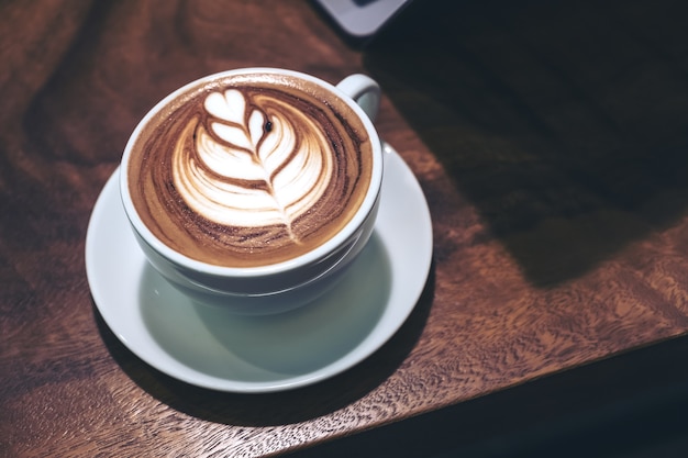 Closeup imagem de uma xícara de café com leite quente com arte de latte de coração e laptop