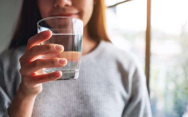 Closeup imagen de una hermosa joven asiática sosteniendo un vaso de agua para beber