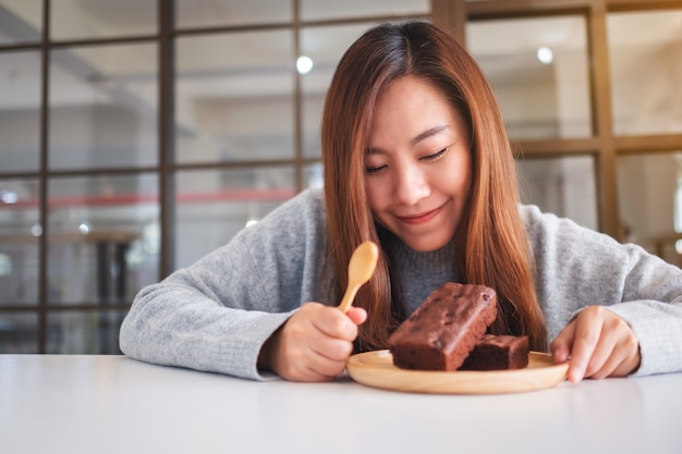 Closeup imagen de una hermosa mujer asiática mirando y comiendo delicioso pastel de brownie en placa de madera