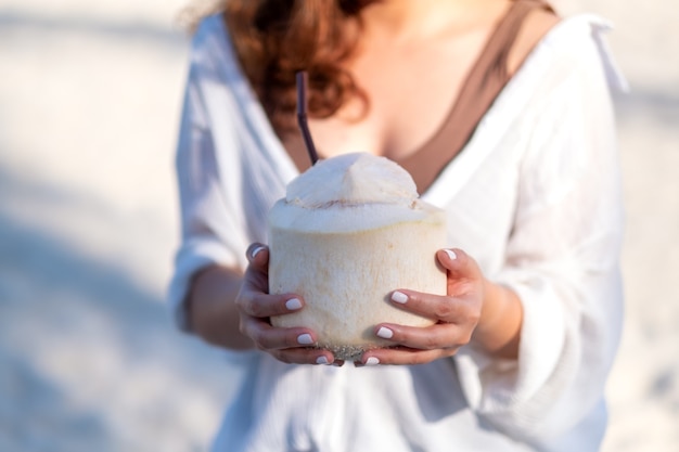 Closeup imagen de una hermosa mujer asiática sosteniendo y bebiendo jugo de coco en la playa