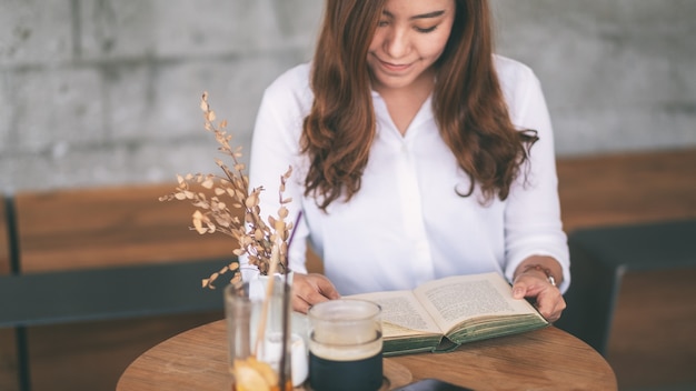 Foto closeup imagen de una hermosa mujer asiática sosteniendo y leyendo un libro mientras está sentado en la cafetería