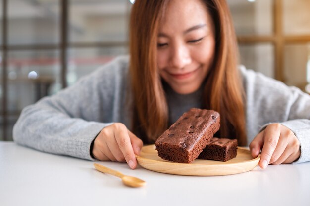 Closeup imagen de una hermosa mujer asiática sosteniendo y mirando pastel de brownie en placa de madera