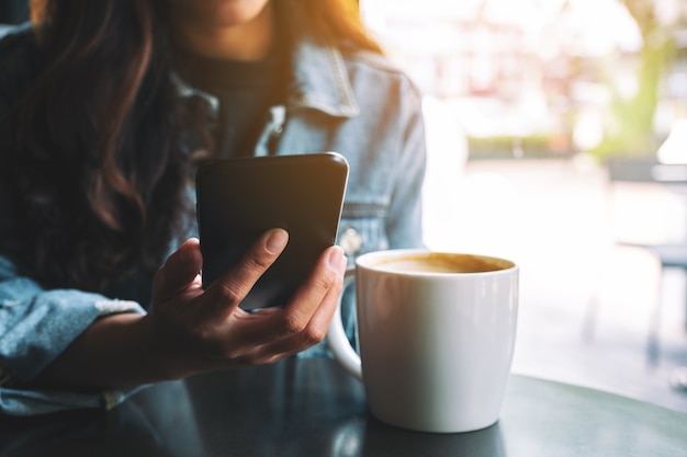 Closeup imagen de una hermosa mujer asiática sosteniendo y usando un teléfono móvil con una taza de café sobre la mesa