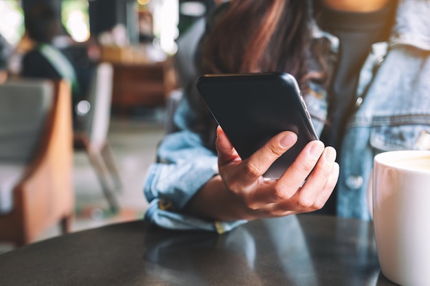 Closeup imagen de una hermosa mujer asiática sosteniendo y usando un teléfono móvil con una taza de café sobre la mesa