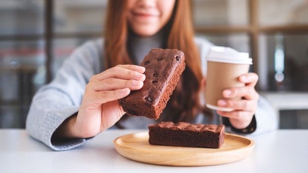 Closeup imagen de una hermosa mujer sosteniendo y comiendo un trozo de tarta de brownie mientras bebe café