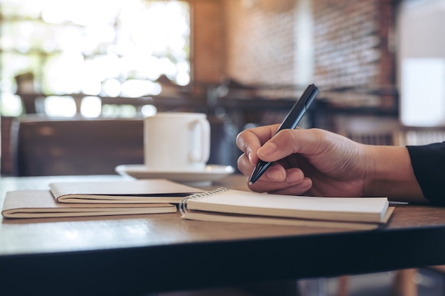 Closeup imagen de una mano escribiendo en un cuaderno en blanco con una taza de café en la mesa de café