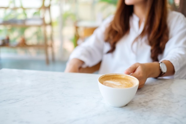 Closeup imagen de una mujer agarrando una taza de café caliente sobre la mesa