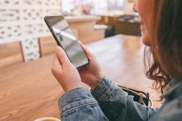 Closeup imagen de una mujer asiática sosteniendo, usando y mirando el teléfono inteligente en la cafetería