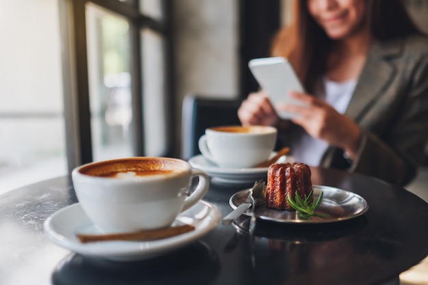 Closeup imagen de una mujer asiática sosteniendo y usando un teléfono móvil con tazas de café y bocadillos en la mesa de café