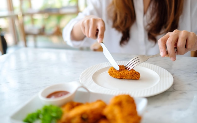 Closeup imagen de una mujer con cuchillo y tenedor para comer pollo frito en restaurante.