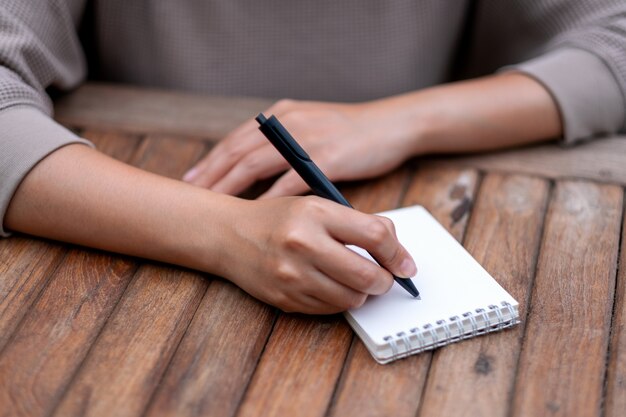 Closeup imagen de una mujer escribiendo en un cuaderno en blanco sobre la mesa de madera