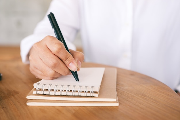 Closeup imagen de una mujer escribiendo en un cuaderno en blanco sobre la mesa de madera