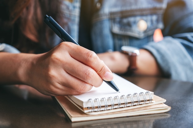 Closeup imagen de una mujer escribiendo en un cuaderno en blanco sobre la mesa