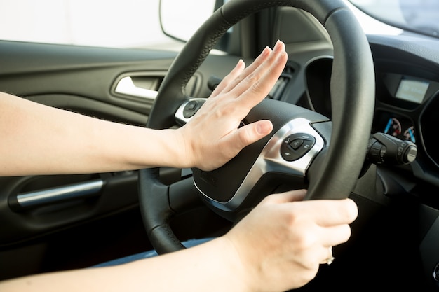 Closeup imagen de mujer molesta conduciendo coche y tocando la bocina