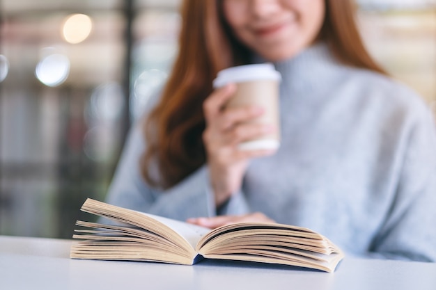 Closeup imagen de una mujer sosteniendo y leyendo un libro mientras bebe café en la mesa de madera