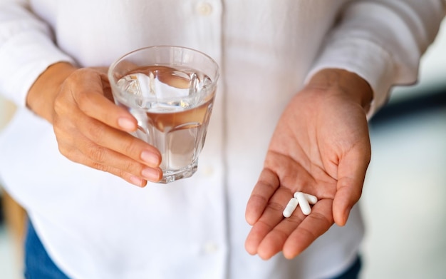 Closeup imagen de una mujer sosteniendo pastillas blancas y un vaso de agua