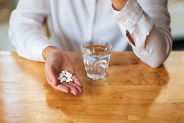 Closeup imagen de una mujer sosteniendo pastillas blancas y un vaso de agua