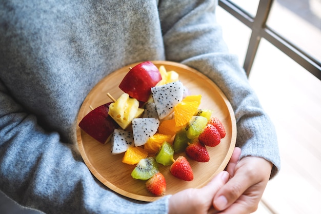 Closeup imagen de una mujer sosteniendo una placa de madera de frutas frescas mixtas en brochetas