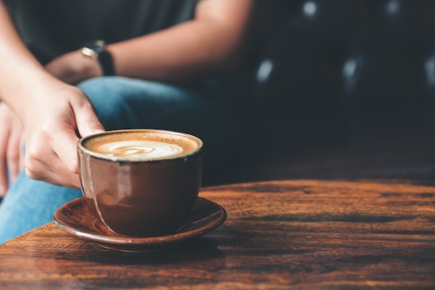 Closeup imagen de una mujer sosteniendo una taza de café en la mesa de madera vintage en cafe