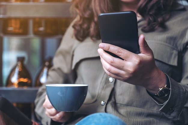 Closeup imagen de una mujer sosteniendo, usando y mirando el teléfono inteligente mientras bebe café en la cafetería