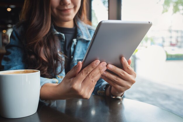 Closeup imagen de una mujer sosteniendo y usando tablet pc con taza de café sobre la mesa