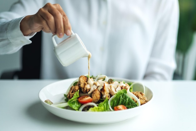 Closeup imagen de una mujer vertiendo aderezo en una ensalada de pollo