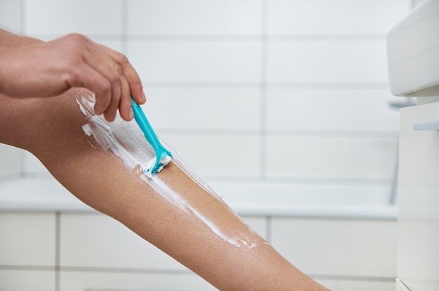 Closeup imagen de la pierna de la mujer joven con crema de afeitar y hoja de afeitar en la mano