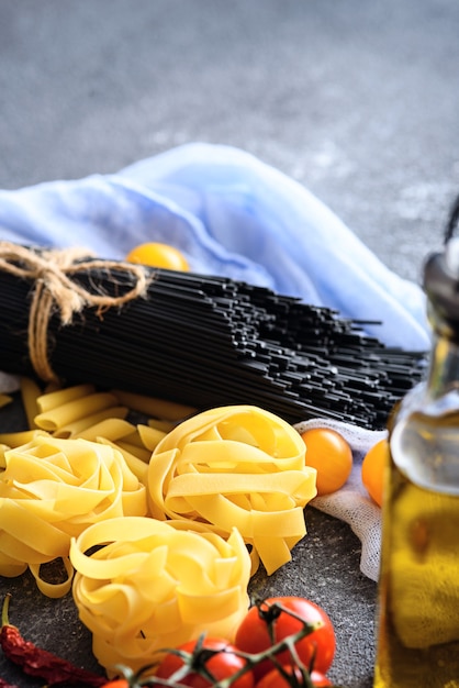 Closeup imagen vertical de ingredientes de comida italiana, pasta, espaguetis negros, tomates, aceite de oliva sobre fondo gris, concepto de cena de cocina