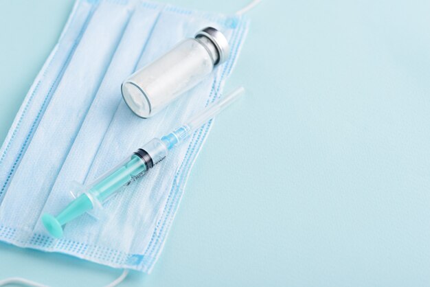 Closeup jeringa médica, ampolla de vidrio, máscara médica sobre fondo azul, vacunación, concepto de inoculación, espacio de copia