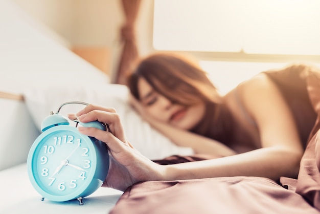 Foto closeup jovem mulher dormindo e levantar a mão para desligar o despertador no quarto em casa