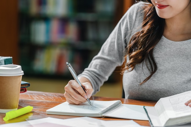 Closeup joven estudiante asiático escribir deberes a mano en la biblioteca de la universidad o colega con varios