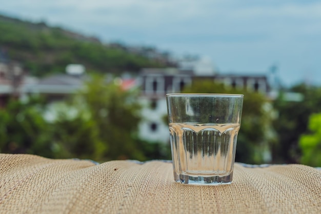 Closeup leeres schäbiges altes Glas mit Kalk Texturierte Bambus-Holzoberfläche Tischset auf dem Balkon Natur grüne Häuser Stadtansicht Hintergrund Dehydration Alkoholismus Beenden von schlechten Gewohnheiten Sucht