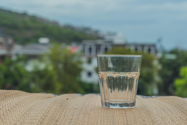 Closeup leeres schäbiges altes Glas mit Kalk Texturierte Bambus-Holzoberfläche Tischset auf dem Balkon Natur grüne Häuser Stadtansicht Hintergrund Dehydration Alkoholismus Beenden von schlechten Gewohnheiten Sucht