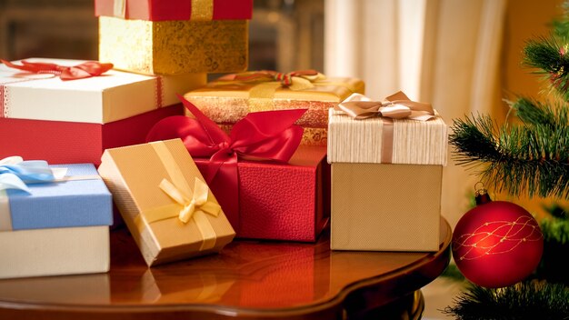 Closeup linda foto de uma grande pilha de presentes de Natal e presentes em caixas de pé na mesa de madeira na sala de estar contra a árvore de Natal e a lareira