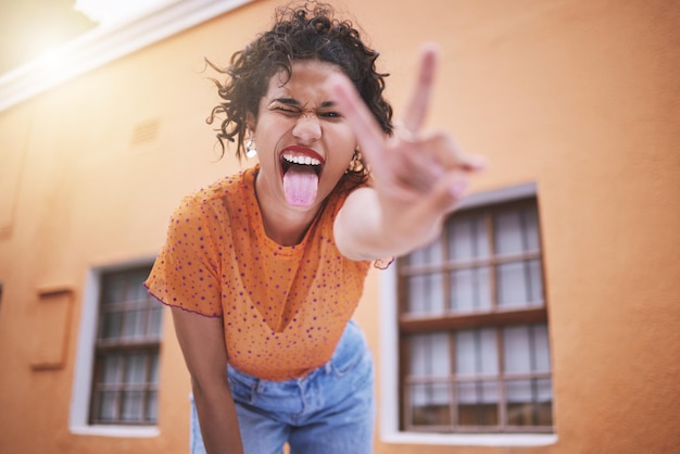 Closeup linda mulher de moda de raça mista fazendo beicinho e gesticulando paz contra um fundo de parede laranja na cidade Jovem mulher hispânica feliz olhando elegante e moderno Despreocupado e elegante