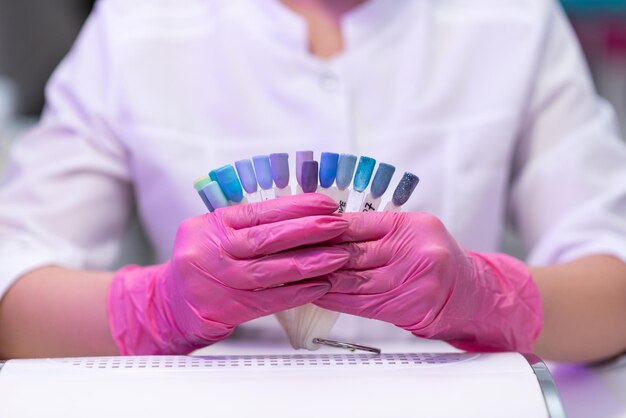 Closeup Manicure em luvas cor de rosa mostra uma paleta de amostras de esmalte para um cliente A garota faz uma manicure em um salão de beleza Cuidados com as unhas Procedimentos cosméticos