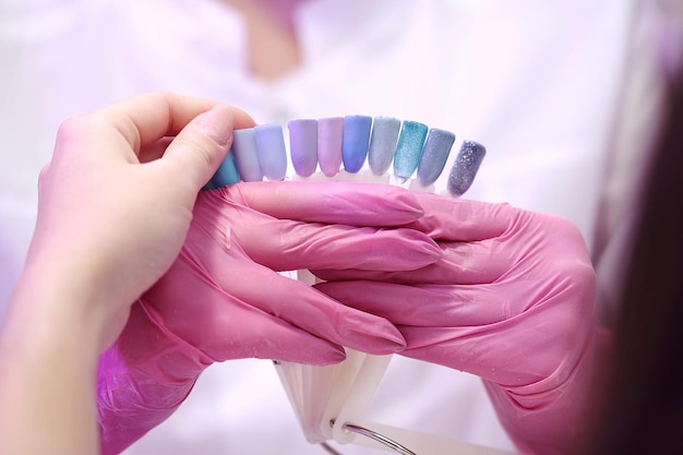 Closeup Manicure em luvas cor de rosa mostra uma paleta de amostras de esmalte para um cliente A garota faz uma manicure em um salão de beleza Cuidados com as unhas Procedimentos cosméticos