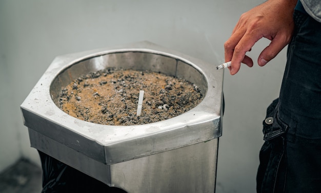 Closeup mano de un hombre con cigarrillo. La gente fumaba en la zona de fumadores del centro comercial y dejaba el cigarrillo en el cenicero. Dejar de fumar o dejar de fumar y cáncer de pulmón.